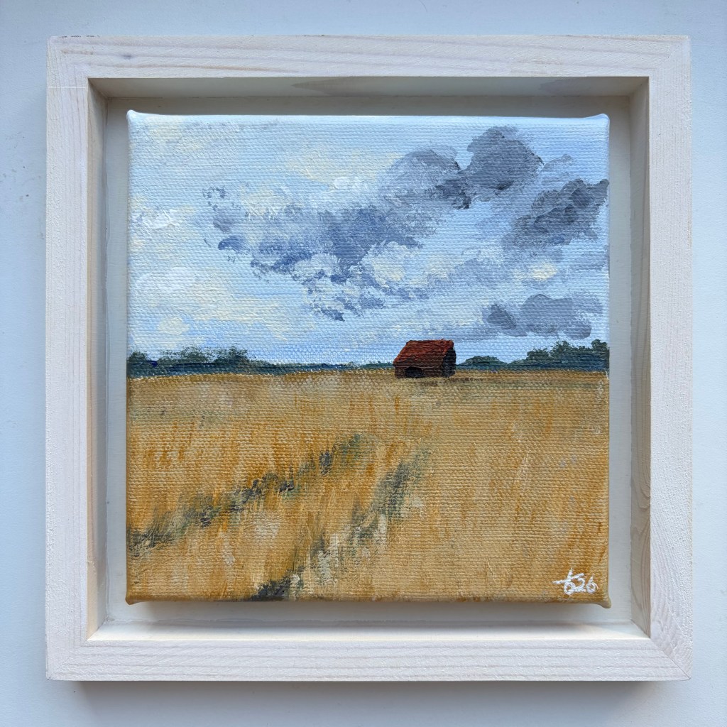 Miniature acrylic painting of a golden field with a small red-roofed barn and cloudy blue-grey sky, presented in a white wooden floating frame.