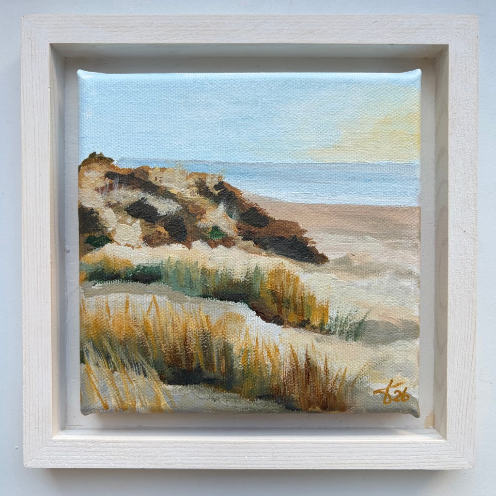 Miniature acrylic painting of sandy coastal dunes with golden grasses, low vegetation and a calm blue sea, presented in a white wooden floating frame.